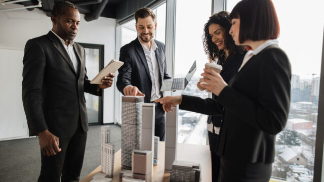 Multiethnic real estate agents, standing near table with city model in office with panoramic view